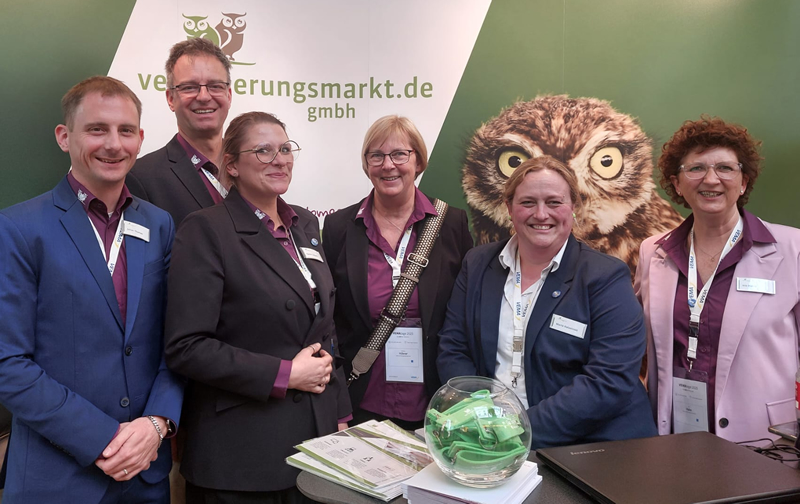 Gruppenfoto von sechs Personen am Messestand von „vermessungsmarkt.de“, mit einem Eulenmotiv im Hintergrund.